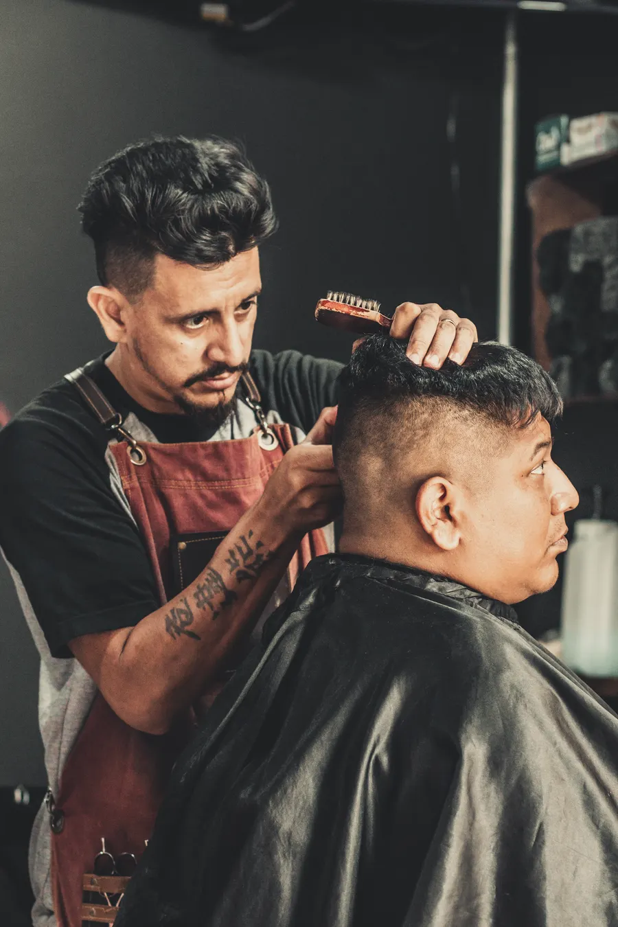 Dante Rivera in a leather apron styling a client’s hair with a brush